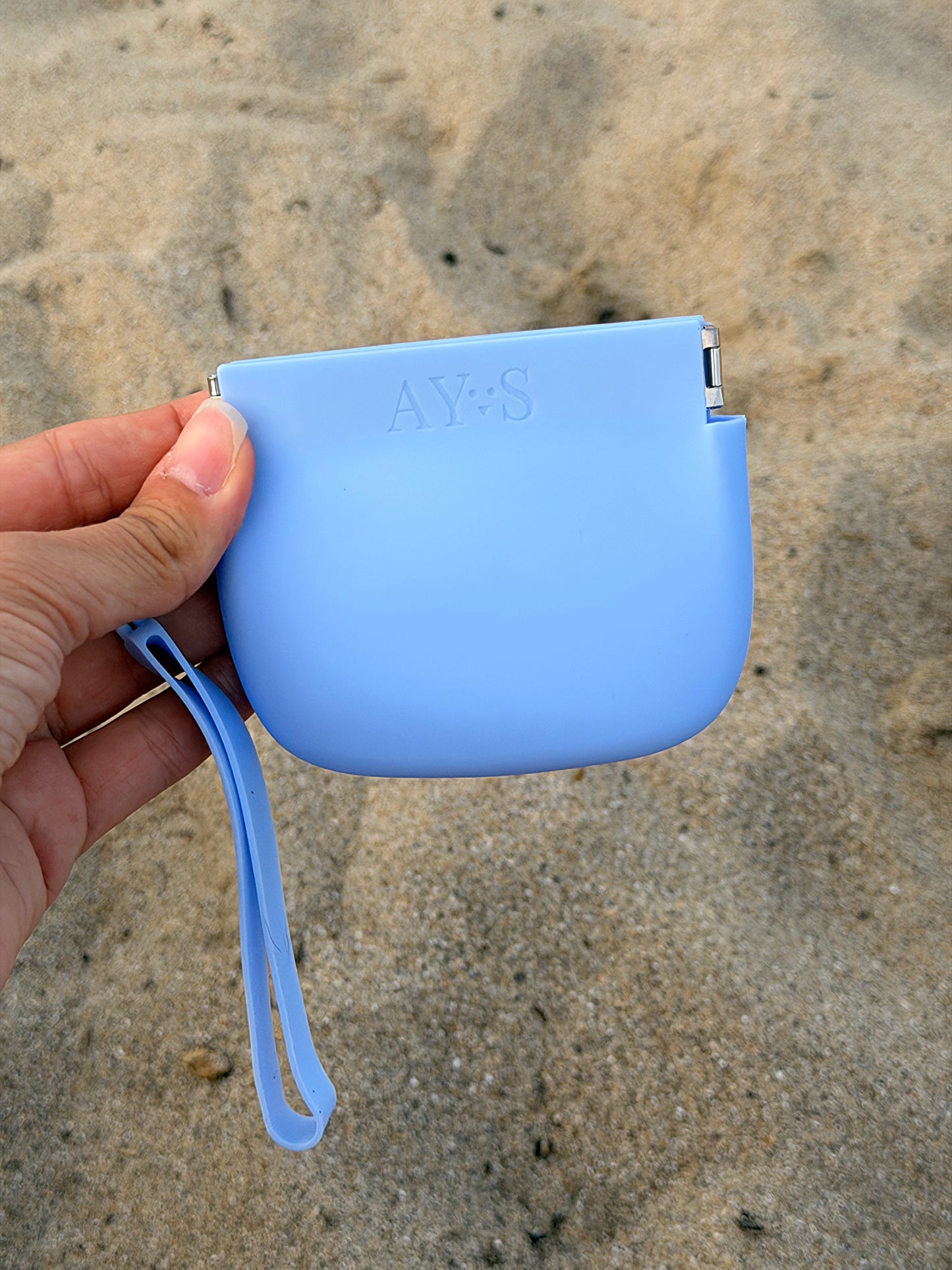 Pochette à friandises en silicone bleu AYOS Club tenue à la main sur une plage, idéale pour les promenades et les séances d’éducation avec son chien.