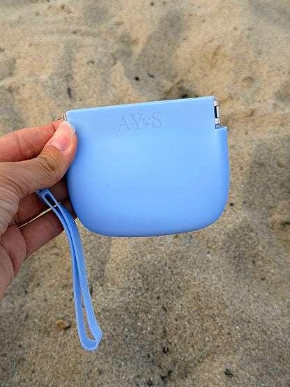 Pochette à friandises en silicone bleu AYOS Club tenue à la main sur une plage, idéale pour les promenades et les séances d’éducation avec son chien.