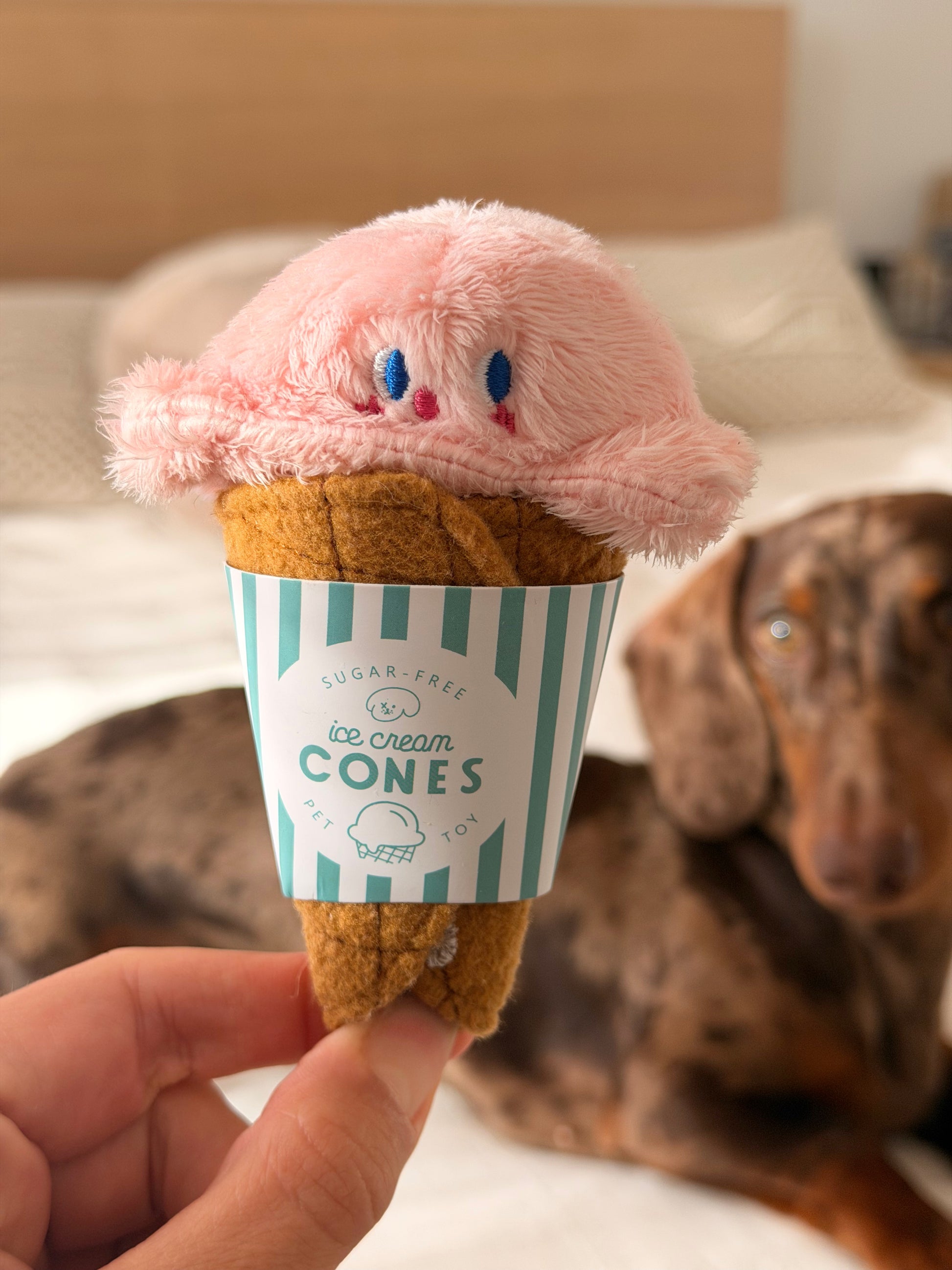 Gelato Toy pour chien, jouet cache-friandises rose en forme de glace avec teckel en arrière-plan.