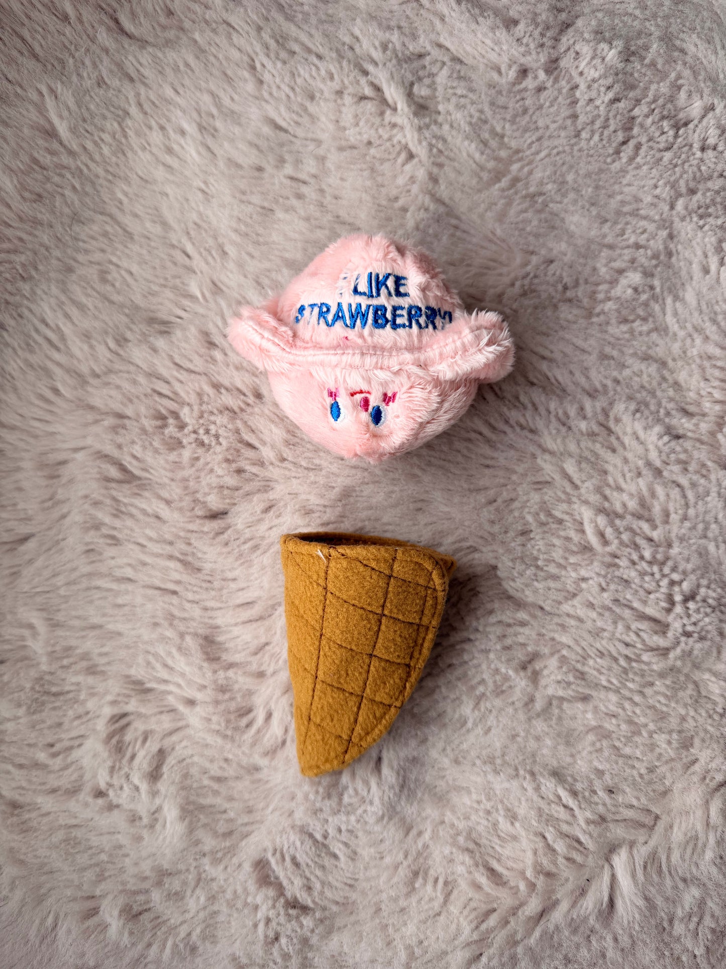 Jouet interactif pour chien en forme de glace rose et cône cache-friandises séparés sur plaid beige doux, conçu pour l’occupation et la stimulation mentale des chiens.