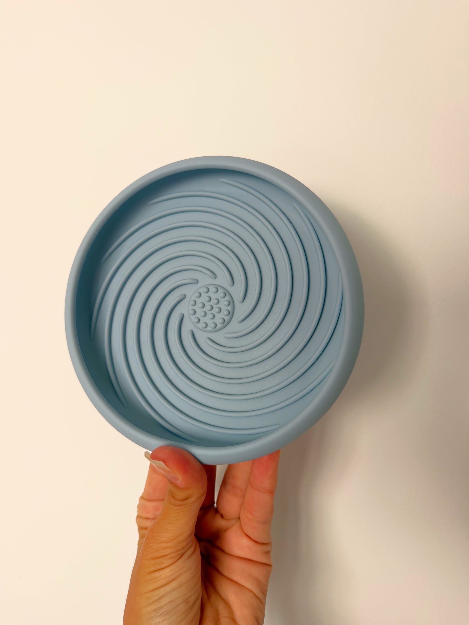 Le Nuage Bowl bleu ciel, tapis de léchage en silicone pour chien, tenu en main afin d’illustrer sa taille et sa texture spiralée favorisant un léchage lent et apaisant.