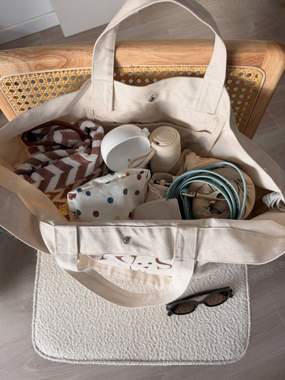 Intérieur du weekender AYOS Club écru rempli d’essentiels pour chien, avec couverture, gourde, gamelle pliable, laisse et accessoires.