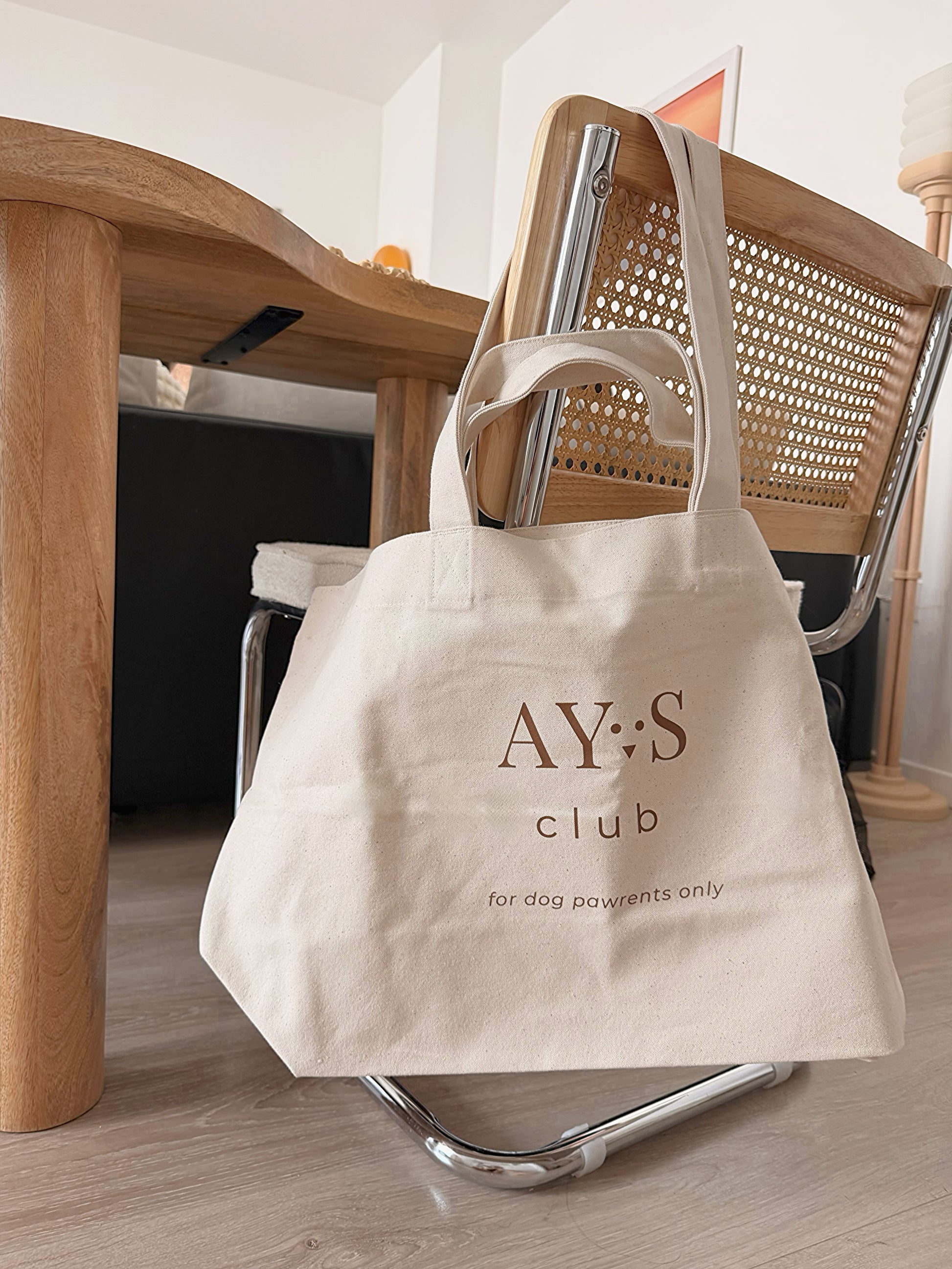 Sac Weekender AYOS Club en toile écrue avec logo marron, posé sur une chaise