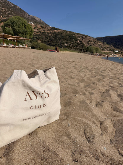 Sac Weekender AYOS Club écru posé sur le sable au bord de la mer, idéal pour les escapades avec son chien